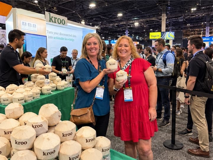 Two attendees holding branded coconuts in front of a table stacked with them
